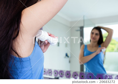 Smiling brunette putting deodorant on her armpit 20683272