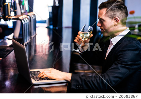 Businessman getting a glass of wine and using laptop 20683867