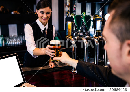 Barmaid serving a pint to customer with laptop 20684438