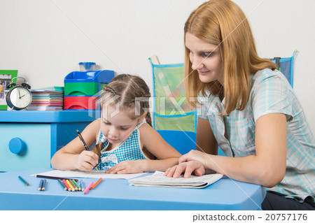 The girl draws in a notebook with a ruler, the teacher helps her The girl draws in a notebook with a ruler, the teacher helps her 20757176