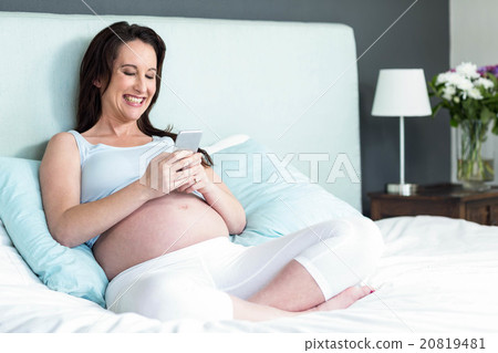 Pregnant woman lying in bed texting 20819481
