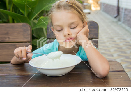 Upset six year old girl looking sadly at the semolina in a spoon at breakfast 20972533