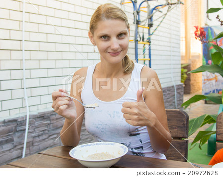 Twenty-five girl eating cereal breakfast on the veranda and shows class Twenty-five girl eating cereal breakfast on the veranda and shows class 20972628