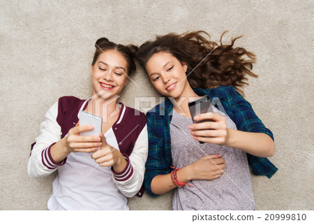 happy teenage girls lying on floor with smartphone happy teenage girls lying on floor with smartphone 20999810