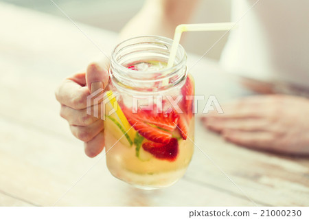 close up of woman holding glass with fruit water 21000230