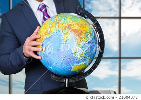 Businessman holds globe near window. 21004378