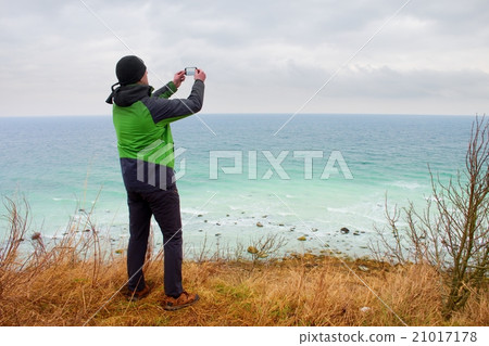 Man in waterproof jacket takes photo of coastline Man in waterproof jacket takes photo of coastline 21017178