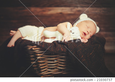 Cute newborn baby in bear hat sleeps in basket with toy teddy be Cute newborn baby in bear hat sleeps in basket with toy teddy be 21030737