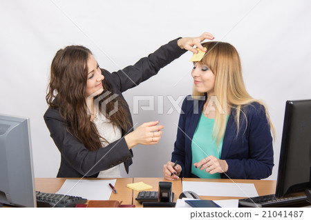 An employee of the office glues note with the drawn sun on the forehead of his colleague 21041487