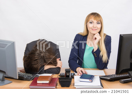 frustrated woman lay on the table, her colleague happily looks into the frame 21041501