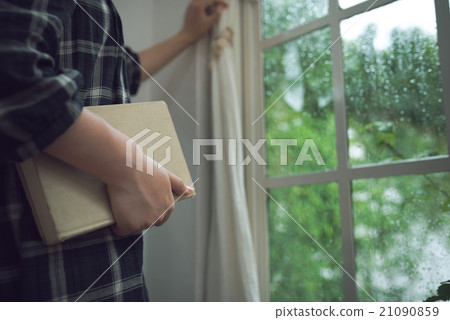 A person reading a book by the window on a rainy day. A person reading a book by the window on a rainy day. 21090859