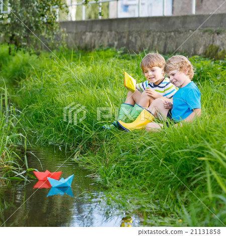 Two little brothers playing with paper boats by a 21131858