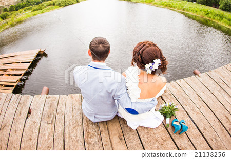 Beautiful young wedding couple sitting on the pier Beautiful young wedding couple sitting on the pier 21138256