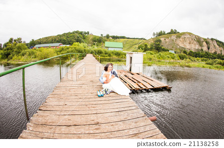 Beautiful young wedding couple sitting on the pier Beautiful young wedding couple sitting on the pier 21138258