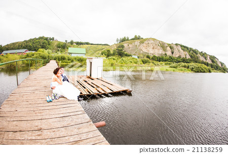Beautiful young wedding couple sitting on the pier Beautiful young wedding couple sitting on the pier 21138259