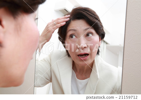 A woman in her 60's who checks her hair with a mirror 21159712