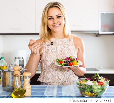 girl standing at kitchen table with plate of salad 21215331