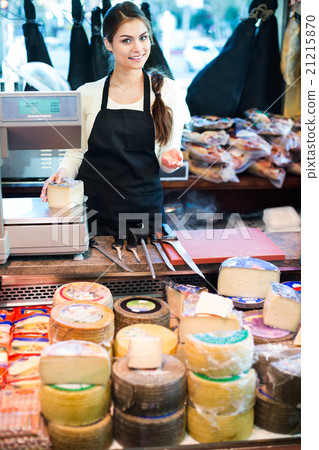 Cheerful young shopgirl selling cheese Cheerful young shopgirl selling cheese 21215870