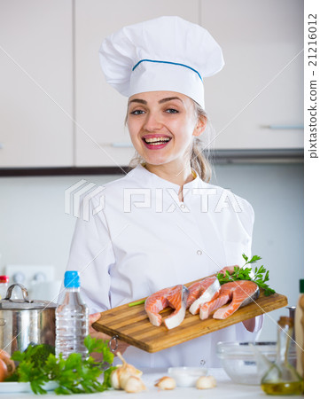 Happy female cook posing with salmon fillets in kitchen 21216012