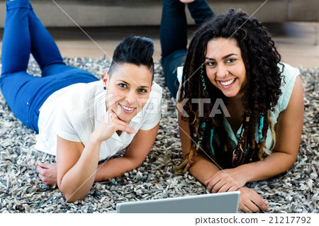Portrait of lesbian couple lying on rug and using laptop 21217792