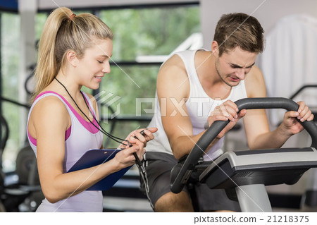 Trainer woman talking with a man doing exercise bike Trainer woman talking with a man doing exercise bike 21218375