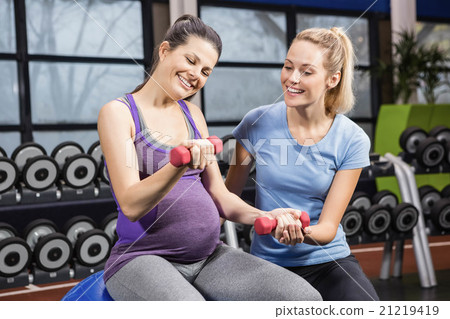 Trainer helping pregnant woman at the gym Trainer helping pregnant woman at the gym 21219419