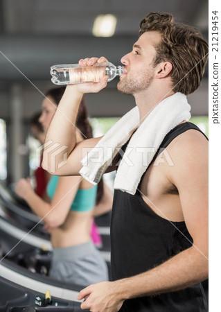 Athletic man drinking water while running on treadmill 21219454