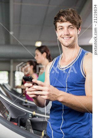 Smiling muscular man on treadmill listening to music 21219834