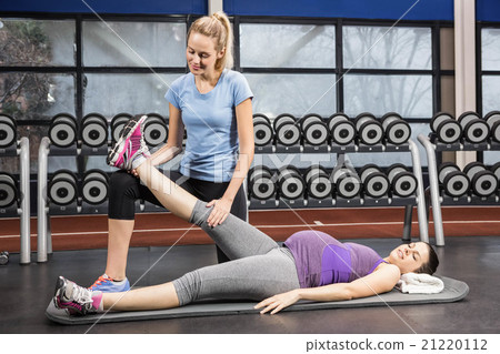 Smiling trainer stretching pregnant womans leg Smiling trainer stretching pregnant womans leg 21220112