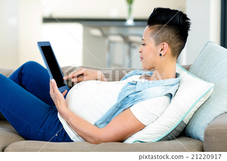 Pregnant woman relaxing on sofa with her digital tablet 21220917
