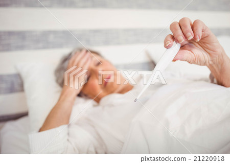 Senior woman checking her temperature 21220918