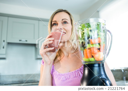 Blonde woman drinking a smoothie in the kitchen Blonde woman drinking a smoothie in the kitchen 21221764