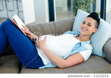 Portrait of pregnant woman reading a book while lying on sofa 21222014
