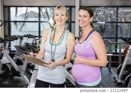 Smiling trainer showing clipboard to pregnant woman Smiling trainer showing clipboard to pregnant woman 21222497