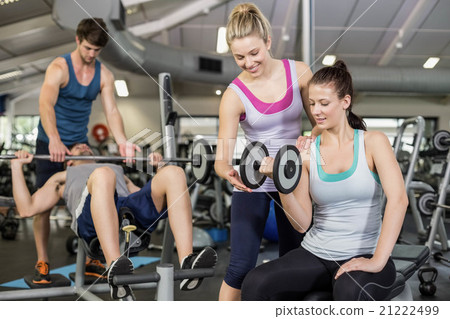 Trainer woman helping woman lifting dumbbell 21222499