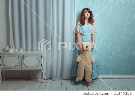 Woman stands near wall with a bear toy. 21245396