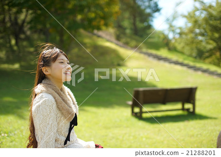 Long hair young woman who sits on a park bench and feels a gentle breeze and is relaxed and heals refreshingly Long hair young woman who sits on a park bench and feels a gentle breeze and is relaxed and heals refreshingly 21288201