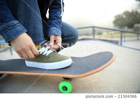 skateboarder tying shoelace at skatepark 21304366