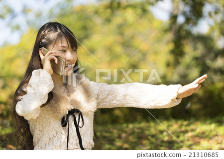 愉快地談話與智能手機在一個綠色森林公園女學生與揮動手的逗人喜愛的微笑,當談話時 愉快地談話與智能手機在一個綠色森林公園女學生與揮動手的逗人喜愛的微笑,當談話時 21310685