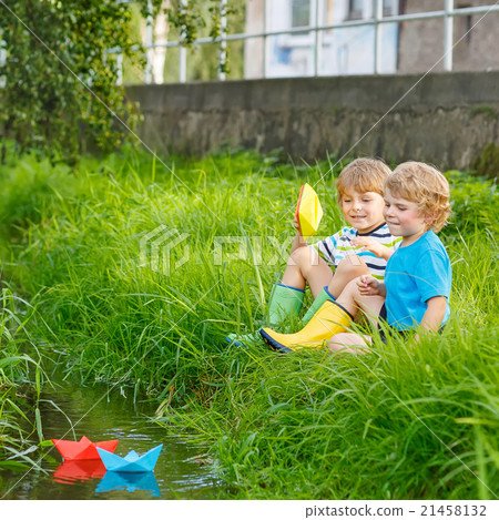 Two little brothers playing with paper boats by a 21458132