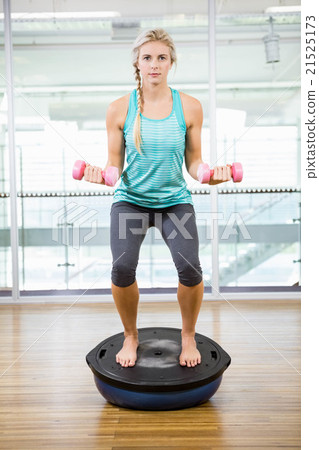 Fit blonde standing on bosu ball and lifting dumbbells 21525173