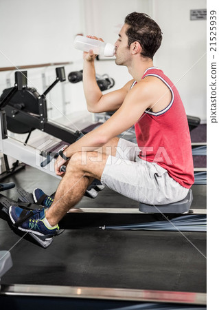 Muscular man on rowing machine drinking water 21525939