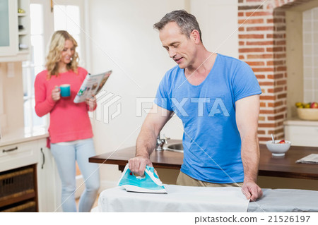 Man using iron while wife reading the news 21526197