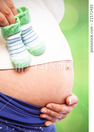 Composite image of pregnant woman holding baby shoes over bump 21572485