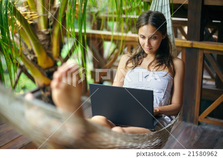Woman lying in a hammock with laptop in a tropical Woman lying in a hammock with laptop in a tropical 21580962