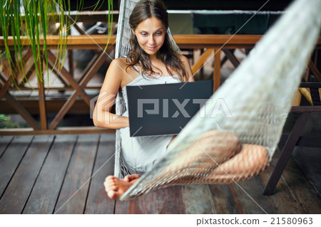 Woman lying in a hammock with laptop in a tropical Woman lying in a hammock with laptop in a tropical 21580963