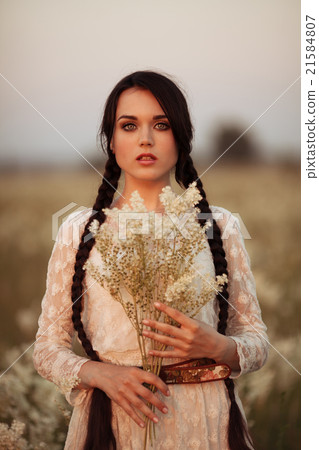 Young girl with long dark hair holding white flowers at the spring field. 21584807