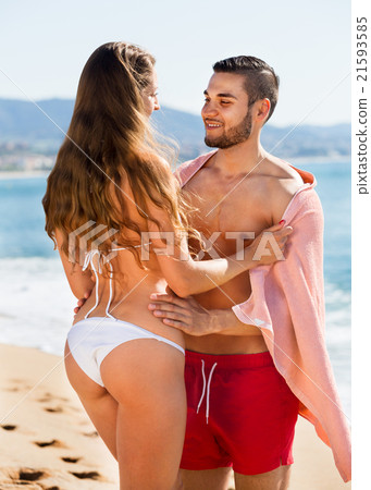 Happy couple standing in towel at sea coast 21593585