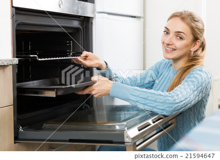 girl putting baking tray in kitchen oven 21594647