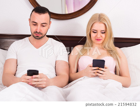 Couple with phones in bed. 21594832